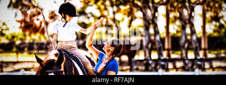 Side view of woman giving high five to girl sitting on horse Stock Photo