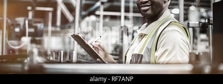 Portrait of smiling factory worker writing on clipboard in factory Stock Photo