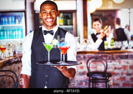 Portrait of bartender holding serving tray with cocktail glasses Stock Photo