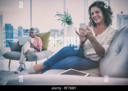 Smiling woman using smartphone by man sitting at home Stock Photo
