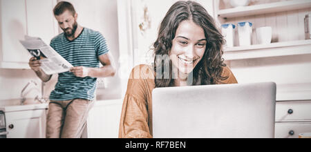 Woman using laptop while man reading newspaper in background Stock Photo