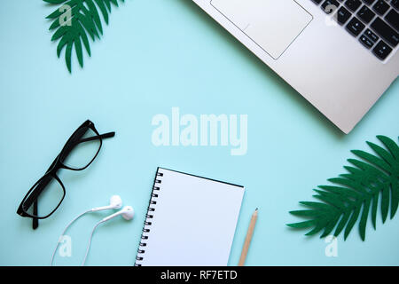 Workspace in a trendy blue color. Many different items including a laptop, glasses, notebook, and headphones are on the table. Stock Photo