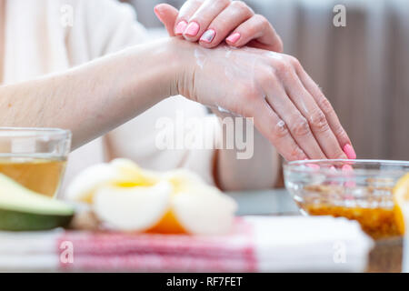 The woman applying the cream on her hands moisturizing and nourishing them with natural cosmetics close-up. Concept of hygiene and care for the skin Stock Photo