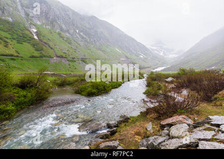 Passo del San Gottardo or St. Gotthard Pass summer misty landscape with water stream (Switzerland). Rainy weather. Stock Photo