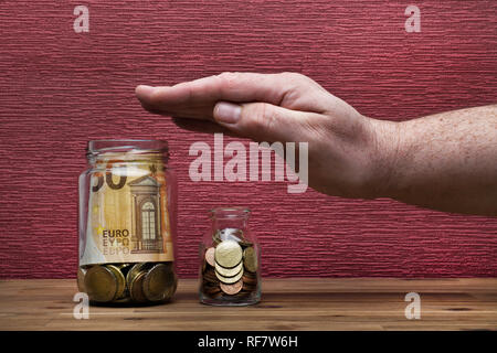 Hand protects euro coins and bill on the burgundy red background in a money box, isolated on the table Stock Photo