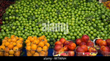 Fresh green pulms, fresh loquats, fresh nectarines. Various fresh fruits on the market counter. Some in pile, some in plastic packages. Stock Photo
