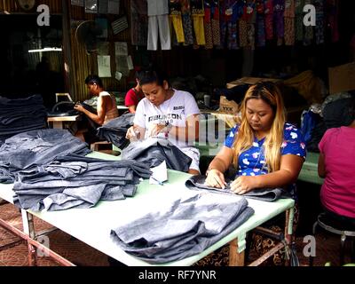 ANTIPOLO CITY, PHILIPPINES - JANUARY 7, 2019: Tailors at a clothes manufacturing company put finishing touches on long denim pants. Stock Photo
