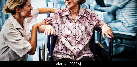 Cheerful disabled senior woman sitting on wheelchair looking at female doctor Stock Photo