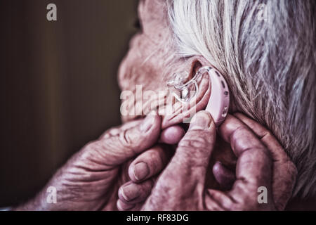 Doctor inserting hearing aid in senior patient ear Stock Photo