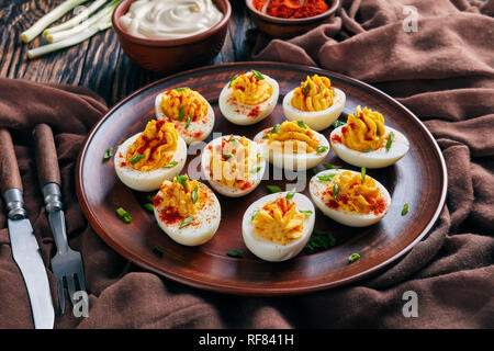 close-up of Deviled Eggs sprinkled with paprika and finely chopped green onion on an earthenware plate on an old rustic wooden table with brown cloth, Stock Photo