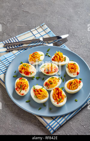 Deviled Eggs seasoned with paprika and finely chopped green onion on a grey plate on a concrete table, vertical view from above Stock Photo