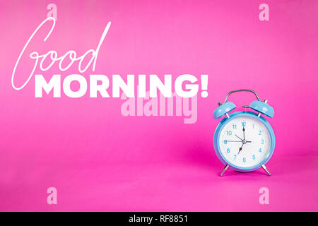 Beautiful blue pastel alarm clock on pink background with quote Good Morning Stock Photo
