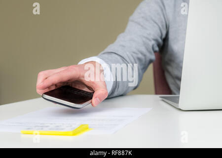 Close up of young business student man using smart phone at workplace. Closeup of hand of man using smartphone at office desk. Men reading a message p Stock Photo
