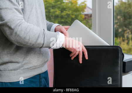Young business man pulling out a laptop out of a leather case at the office Stock Photo
