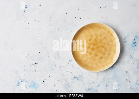 Modern pottery. Yellow dinner plate, Empty ceramic plate with abstract yellow texture on abstract white and blue stucco background. Top view with copy Stock Photo
