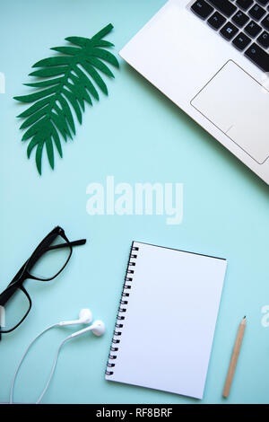 Workspace in a trendy blue color. Many different items including a laptop, glasses, notebook, and headphones are on the table. Stock Photo