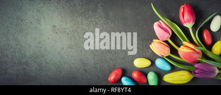 Easter banner with colorful eggs and fresh spring tulips arranged to the side over textured slate with copy space and vignette for your holiday greeti Stock Photo