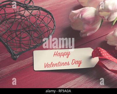 Happy Valentines Day concept with a heart shape and a bunch of pink tulips on a red wooden table Stock Photo