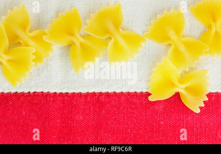 Dry Italian pasta called farfalle on a white-red tablecloth background , beautiful bow tie shape pasta Stock Photo