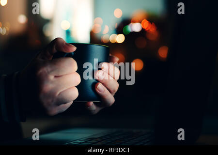 Woman with coffee cup looking at laptop computer at night, close up of hands Stock Photo