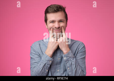 Sad young man dressed in blue shirt makes faces trying to stay optimistic Stock Photo