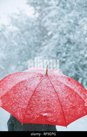 Woman under red umbrella in snow enjoying the first snowfall of the winter season Stock Photo