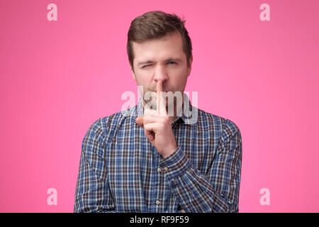 Serious good looking male keeps fore finger on lips, tries to keep conspiracy, Stock Photo