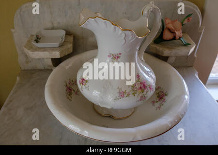 Vintage ceramic water pitcher with basin. Scalloped rim with gold edges and pink floral design. On marble table. Stock Photo