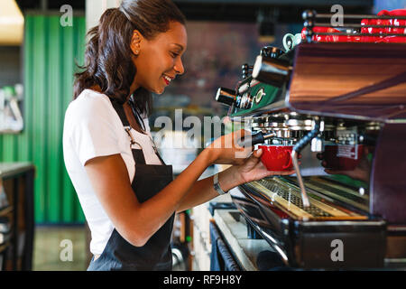 Side view of a smiling female barista making coffee at a cafe Stock Photo