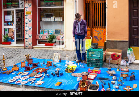 An old​ man in a stylish hat and scarf selling secondhand items at the Jueves Market on Calle Feria in Seville, Spain Stock Photo