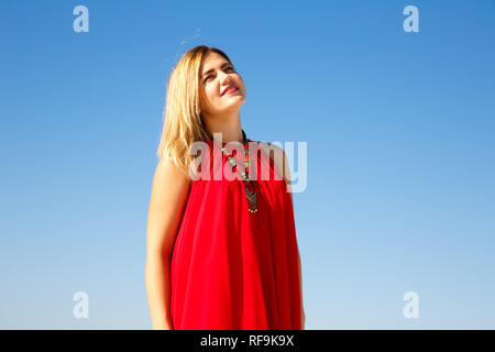 Blond woman in the red dress on the blue sky background. Stock Photo