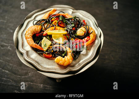 fresh, delicious black spaghetti with grilled prawns, tomatoes, chilli pepper, on an old silver plate Stock Photo