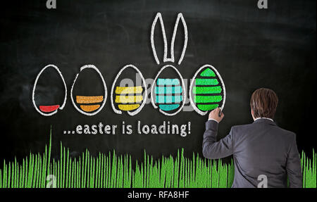 Businessman paints with chalk Easter concept on blackboard. Stock Photo