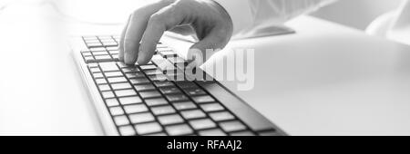 Wide view black and white image of male hand typing on computer keyboard. Stock Photo