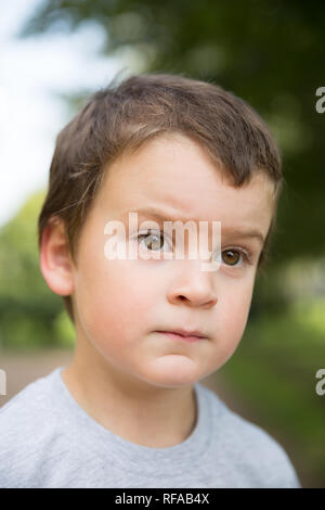Closeup portrait of thinking freckled boy with dark hair and brown eyes outdoors Stock Photo