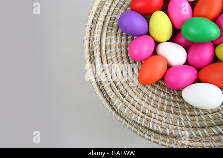 Brightly colored easter eggs, in a straw basket against a grey background. Stock Photo