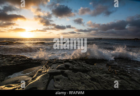 Waves crashing on a rocky beach at sunset Stock Photo