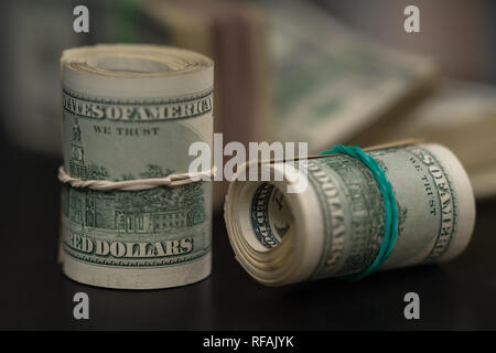 Two rolls of rolled USD bills tied with rubber bands one upright and one on its side on a black table in a conceptual financial or corruption image Stock Photo