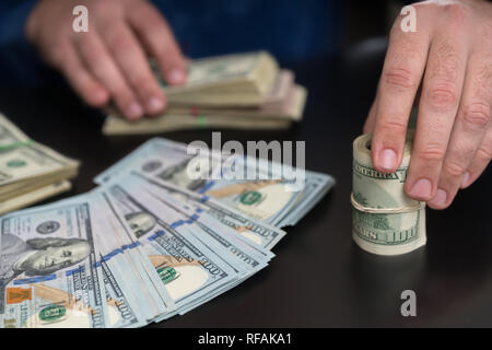 Man passing over a roll of USD banknotes as he counts piles of money in a conceptual financial image close up on his hands Stock Photo
