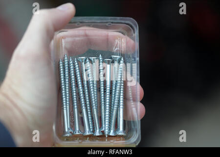 Hand holding container of wood screws used for carpentry and repair work. Stock Photo