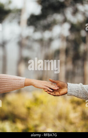 Interracial couple hands reaching to each other outdoors. Couple approaching to each other and holding hands. Stock Photo