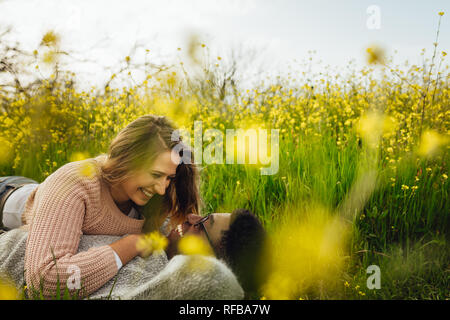 Young woman lying with her boyfriend on the high grass and smiling. Loving couple lying on the grass looking at each other and smiling. Stock Photo