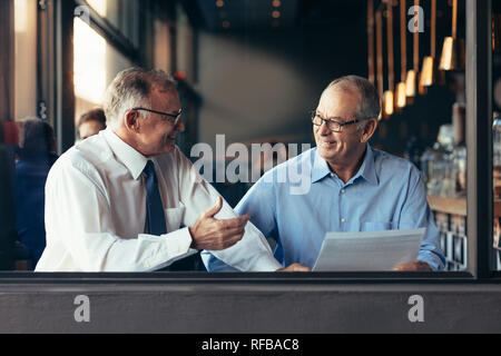 Senior business man with male colleague working together in modern restaurant. View from through window glass of two mature business partners working Stock Photo