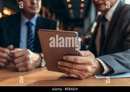 Close up of digital tablet in hand of businessman talking to his partner. Two businessman meeting at coffee with digital tablet. Focus on table pc. Stock Photo