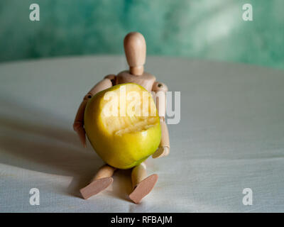 A wooden figurine with a bitten green apple on top of a table Stock Photo