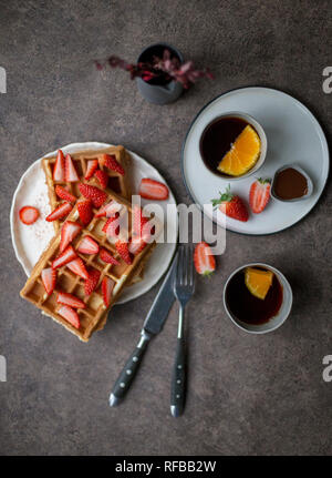 Sweet Belgium waffles with strawberry at white plate and two cup of tea with lemon at dark background. Concept of healthy lifestyle for menu Stock Photo