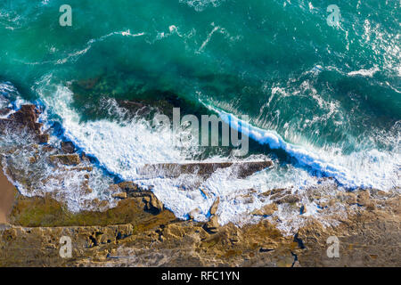 Top down view of the waves crashing onto the rock shelf at Dudley Beach - Newastle Australia. Aerial view of rugged coastal lanscape. Stock Photo