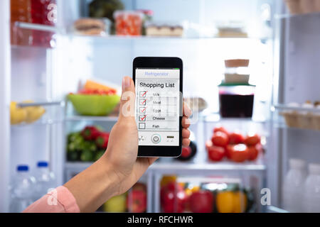 Close-up Of A Woman's Hand Showing Shopping List On Mobile Phone In The Refrigerator Stock Photo