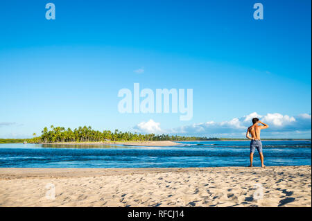 Bright scenic view of a rustic beach on a remote island off the coast of Bahia, Brazil with a solitary figure looking out at the horizon Stock Photo