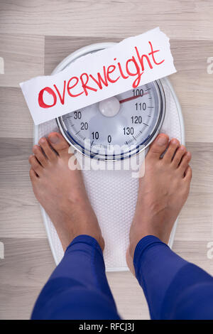 Close-up Of Woman's Feet On Weighing Scale Indicating Overweight On White Paper Stock Photo